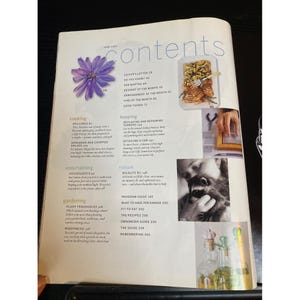 May include: Magazine page with the title "Contents" and various articles. Features include cooking, gardening, and nature sections. Includes images of food, a raccoon, and decorative bottles. The magazine is open on a black surface.