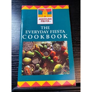 May include: A cookbook titled "The Everyday Fiesta Cookbook" with a teal cover and a colorful border. The cover features the "Mexican Fiesta" logo and a vibrant image of various Mexican food ingredients, including tomatoes, avocados, and spices.