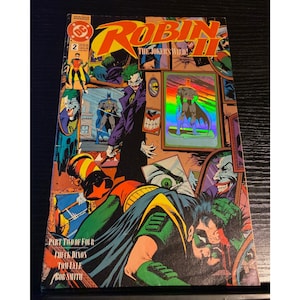 May include: Comic book cover for Robin II: The Joker's Wild #2. The cover features illustrations of Robin, the Joker, and Batman. The comic has a vibrant color palette with text that reads "Robin II" and "The Joker's Wild".