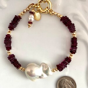 May include: A gold bracelet with a large baroque pearl, red gemstone beads, and a gold clasp. The bracelet is about 7 inches long.