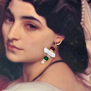 May include: Gold-tone drop earrings featuring a cluster of white, red, green, and pearl-colored beads. The earrings have a unique, asymmetrical design with a gold hook closure. The beads are arranged in a vertical pattern, creating a stylish and eye-catching accessory.