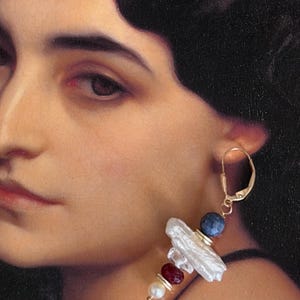 May include: Gold-tone drop earring featuring a white baroque pearl, a blue bead, and red and white gemstones. The earring has a lever back closure and is set against a classical painting background.