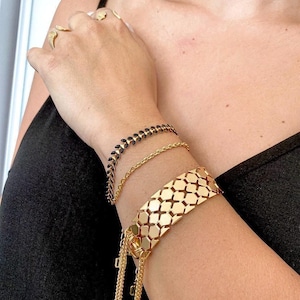 May include: A collection of gold bracelets and rings. The bracelets include a chain link, a black stone and gold chain, and a wide geometric design with dangling chains. The rings have a leaf design.