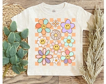 May include: A beige baby onesie with a checkered pattern in peach and white. The onesie features a design of colorful flowers with smiley faces in the center.