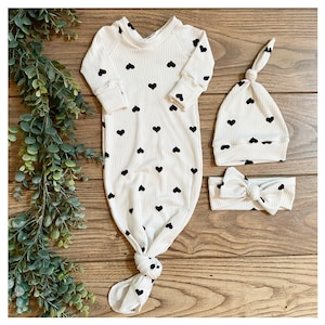 May include: A white knotted gown with black heart print, a matching white hat with black heart print, and a white headband with a black bow.