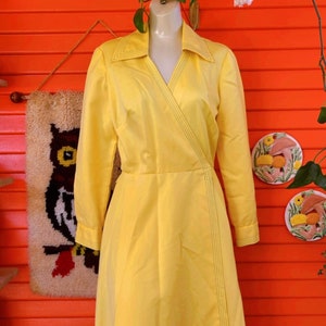 May include: A yellow wrap dress with long sleeves and a V-neckline. The dress has a seam down the front and is made of a smooth fabric.