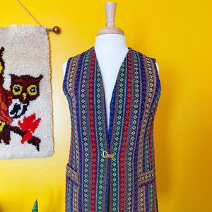 May include: A colorful, striped vest with a geometric pattern in shades of blue, red, green, and yellow. The vest has a V-neck and a gold button closure.