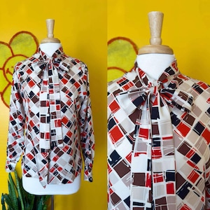 May include: A white, brown, red, and black geometric patterned blouse with a large bow tie at the neck.