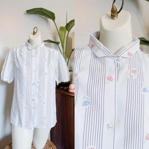 May include: Two white button-down shirts with black vertical stripes and a small floral pattern. One shirt has short sleeves and a peter pan collar, the other has a sleeveless design and a larger collar.