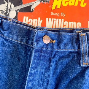 Puede incluir: Primer plano de un par de pantalones vaqueros azules de mezclilla con un bot&oacute;n Wrangler en la cintura.