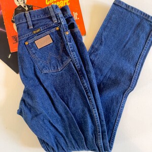 Puede incluir: Un par de pantalones vaqueros de mezclilla azul oscuro con un parche de cuero marr&oacute;n que dice "Wrangler" en el bolsillo trasero.