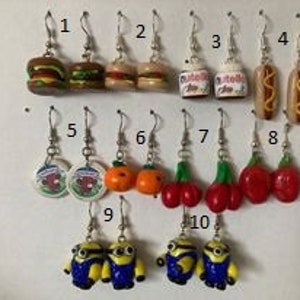 Peut inclure: Dix paires de boucles d'oreilles pendantes représentant différents aliments et personnages de dessins animés. Les boucles d'oreilles sont argentées avec une fermeture à crochet. Les aliments comprennent un hamburger, un hot-dog, une canette de soda, une orange et une cerise. Les personnages de dessins animés sont les Minions.