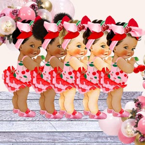 May include: Five baby dolls dressed in pink and red cherry print dresses with ruffled trim. The dolls have brown skin and black hair. They are holding cherries in their hands.