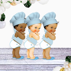 May include: Three baby boy figures wearing blue and white gingham chef hats and matching outfits. The figures are standing in a row on a woodgrain background.