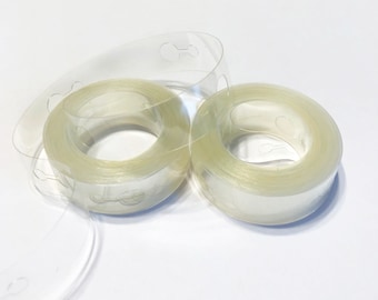 May include: Two rolls of clear balloon tape with adhesive dots for attaching balloons to surfaces. The tape is rolled up and ready to use.