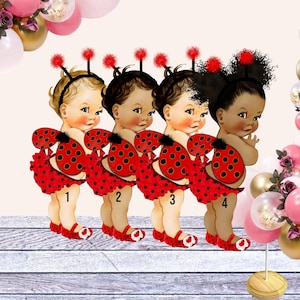 May include: Four baby girl cake toppers dressed as ladybugs. Each topper is wearing a red and black ladybug costume with black polka dots and a red skirt. The toppers are numbered 1 through 4.
