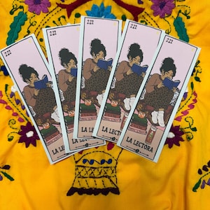 May include: Five rectangular bookmarks featuring a light pink background and an illustration of a person reading a blue book. The text 222 appears at the top, and LA LECTORA is printed at the bottom. The bookmarks are arranged in a fan shape.