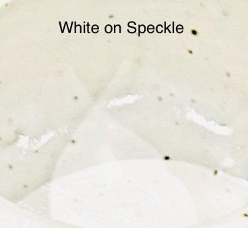 A close-up of a glaze sample labeled "White on Speckle," showing a creamy white glaze with small dark speckles.