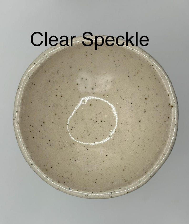 Overhead view of a light beige ceramic bowl with small dark speckles, with the text "Clear Speckle" overlaid.