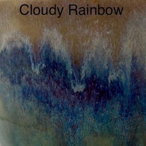 A close-up of a glaze sample labeled "Cloudy Rainbow," showing a top band of tan glaze dripping into mottled blue and purple below.