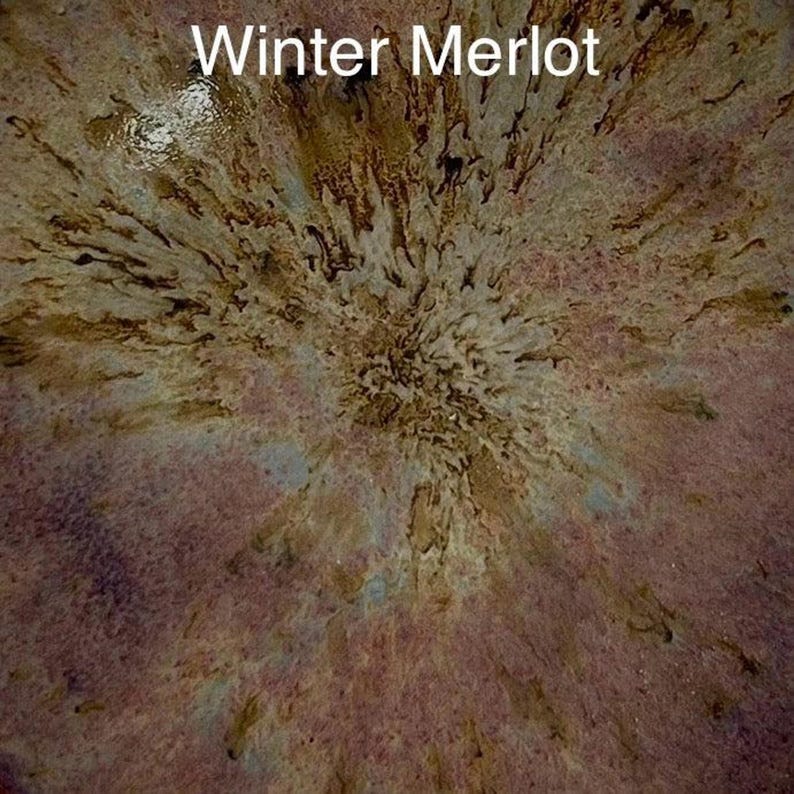 A close-up of a glaze sample labeled "Winter Merlot," featuring a dark reddish-brown with lighter brown and black speckles radiating from the center.