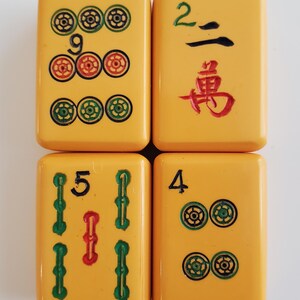 Peut inclure: Quatre tuiles de Mahjong jaunes avec des marquages noirs, verts et rouges. Les tuiles affichent les chiffres 9, 2, 5 et 4, ainsi que des symboles de suite. Les tuiles sont dispos&eacute;es en carr&eacute;.