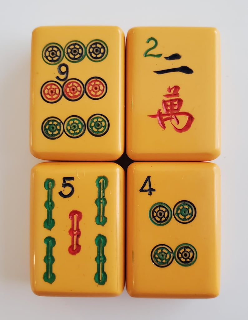 Peut inclure: Quatre tuiles de Mahjong jaunes avec des marquages noirs, verts et rouges. Les tuiles affichent les chiffres 9, 2, 5 et 4, ainsi que des symboles de suite. Les tuiles sont dispos&eacute;es en carr&eacute;.