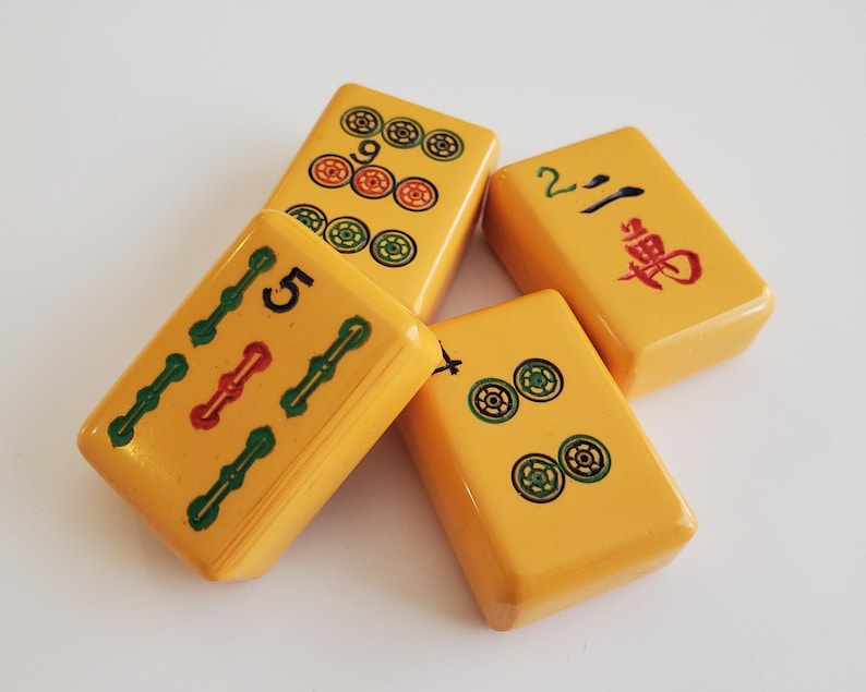 Peut inclure: Quatre tuiles de Mahjong jaunes avec des marquages noirs, rouges et verts. Les tuiles affichent des chiffres, des points et des caract&egrave;res chinois. Les tuiles sont dispos&eacute;es sur une surface blanche.