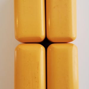 Peut inclure: Quatre objets rectangulaires aux bords arrondis, de couleur jaune chaud, dispos&eacute;s en carr&eacute;. Les objets ont une finition lisse et brillante, sur fond blanc. Ils semblent de taille et de forme similaires.