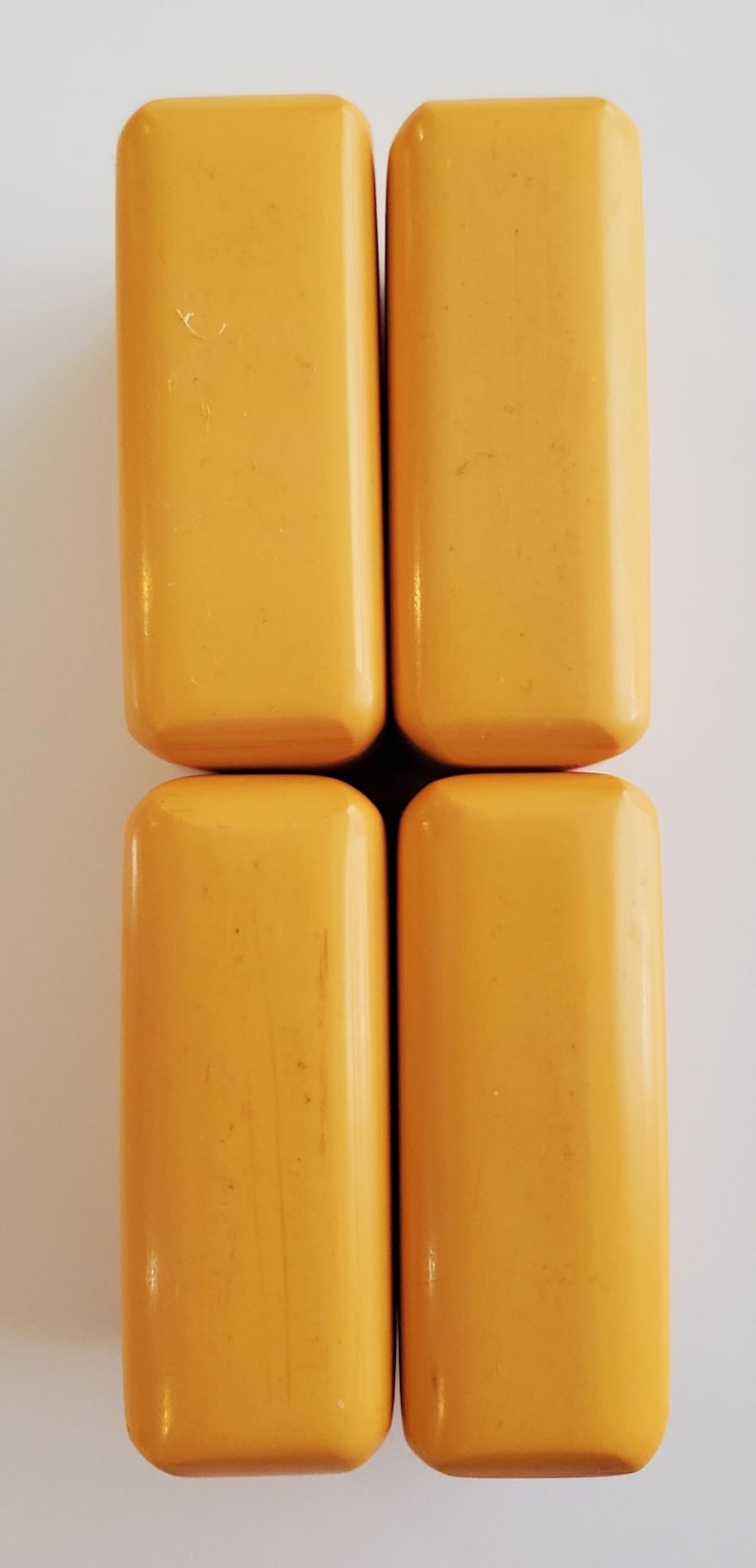Peut inclure: Quatre objets rectangulaires aux bords arrondis, de couleur jaune chaud, dispos&eacute;s en carr&eacute;. Les objets ont une finition lisse et brillante, sur fond blanc. Ils semblent de taille et de forme similaires.