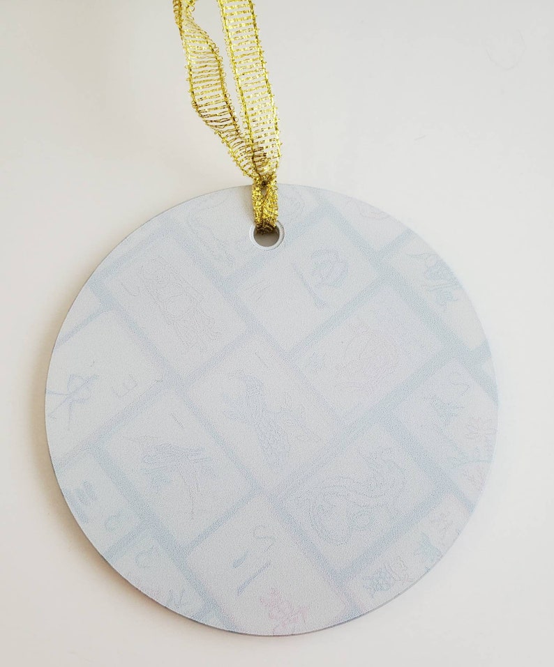 May include: A white round ornament with a gold ribbon attached. The ornament has a hole at the top for hanging and is covered in a light blue pattern.