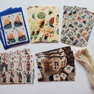 May include: A collection of Mahjong game tiles and accessories. The tiles feature various designs, including boats, figures, and symbols. The set includes blue cardstock, printed cards, and a bundle of twine.