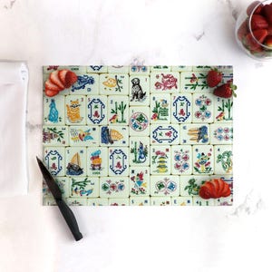 Puede incluir: Una tabla de cortar de vidrio blanco con un dise&ntilde;o colorido de fichas de mahjong. Las fichas presentan varios s&iacute;mbolos, n&uacute;meros y caracteres en rojo, azul, verde y amarillo. La tabla est&aacute; rodeada por un borde blanco.