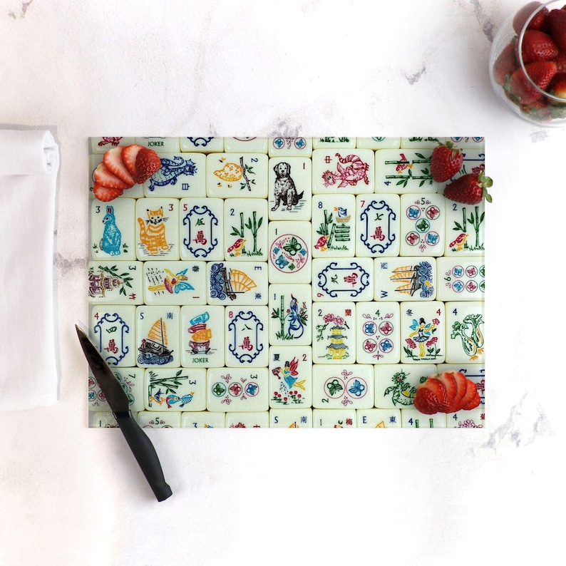 Puede incluir: Una tabla de cortar de vidrio blanco con un dise&ntilde;o colorido de fichas de mahjong. Las fichas presentan varios s&iacute;mbolos, n&uacute;meros y caracteres en rojo, azul, verde y amarillo. La tabla est&aacute; rodeada por un borde blanco.