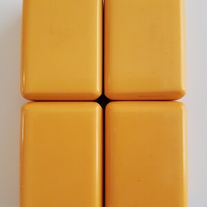 Peut inclure: Quatre tuiles rectangulaires jaune dor&eacute; sont dispos&eacute;es en carr&eacute;. Chaque tuile a des coins arrondis et une surface lisse et brillante. Les tuiles sont espac&eacute;es uniform&eacute;ment sur un fond blanc, cr&eacute;ant un motif g&eacute;om&eacute;trique simple.