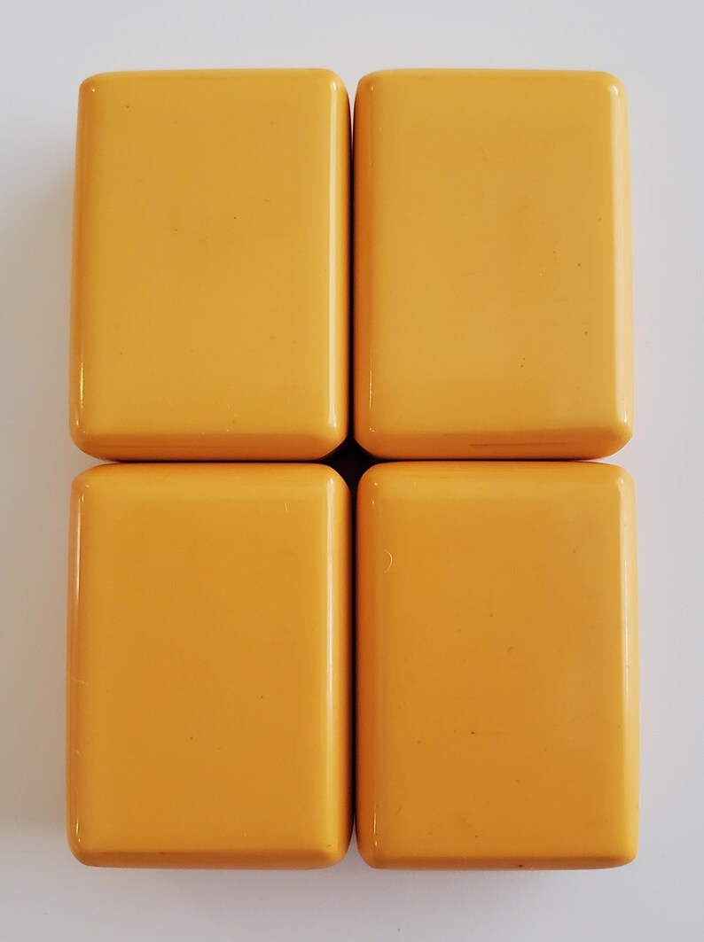 Peut inclure: Quatre tuiles rectangulaires jaune dor&eacute; sont dispos&eacute;es en carr&eacute;. Chaque tuile a des coins arrondis et une surface lisse et brillante. Les tuiles sont espac&eacute;es uniform&eacute;ment sur un fond blanc, cr&eacute;ant un motif g&eacute;om&eacute;trique simple.