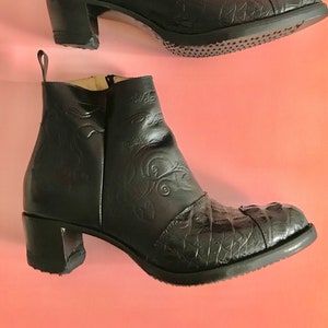 May include: A pair of black leather ankle boots with a crocodile-embossed design. The boots have a block heel and a pointed toe.