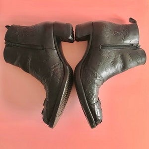 May include: A pair of black leather ankle boots with a decorative floral pattern and a block heel. The boots have a zipper on the inside of each boot.