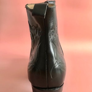 May include: Black leather ankle boots with a decorative floral pattern and a low block heel.