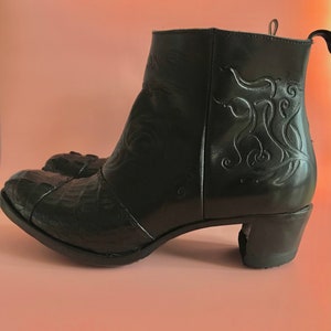 May include: Black leather ankle boots with a decorative floral design on the back. The boots have a low block heel and a pointed toe.