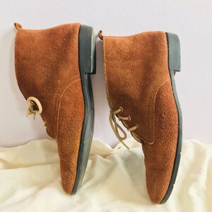 May include: A pair of brown suede ankle boots with laces. The boots have a rounded toe and a low heel.