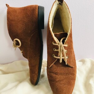 May include: A pair of brown suede ankle boots with laces. The boots have a soft, fuzzy lining.