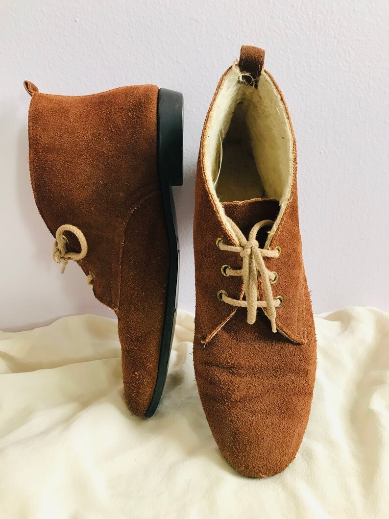 May include: A pair of brown suede ankle boots with laces. The boots have a soft, fuzzy lining.