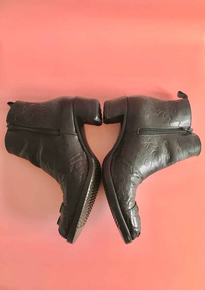 May include: A pair of black leather ankle boots with a decorative floral pattern and a block heel. The boots have a zipper on the inside of each boot.