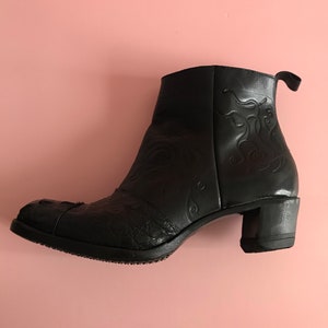 May include: Black leather ankle boots with a decorative floral pattern and a block heel.