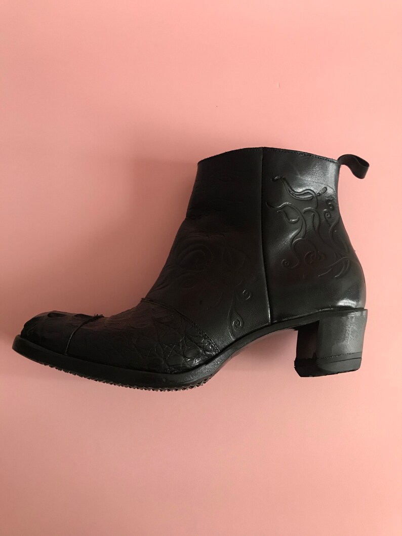 May include: Black leather ankle boots with a decorative floral pattern and a block heel.
