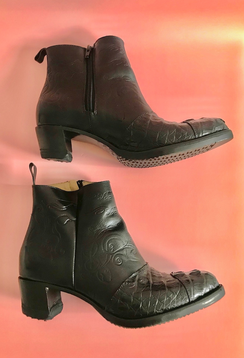 May include: A pair of black leather ankle boots with a crocodile-embossed design. The boots have a block heel and a pointed toe.