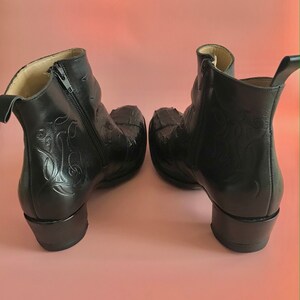 May include: A pair of black leather ankle boots with a zipper on the side and a decorative design on the back. The boots have a block heel.