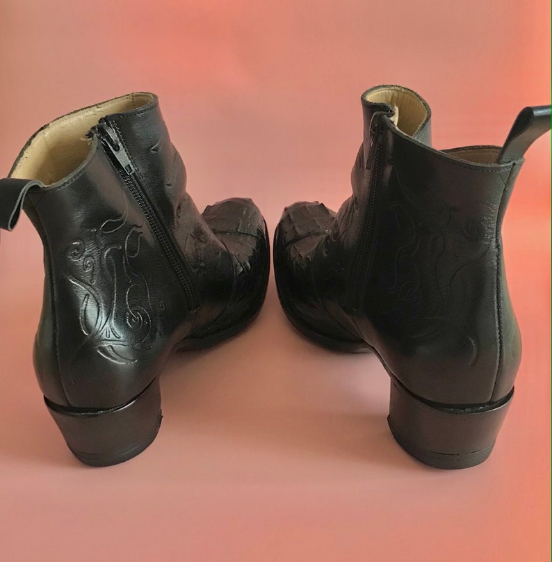 May include: A pair of black leather ankle boots with a zipper on the side and a decorative design on the back. The boots have a block heel.