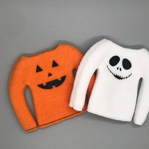 以下が含まれることがあります： ハロウィン用のエルフの衣装2着。1着はオレンジ色でジャック・オー・ランタンの顔、もう1着は白色で幽霊の顔です。